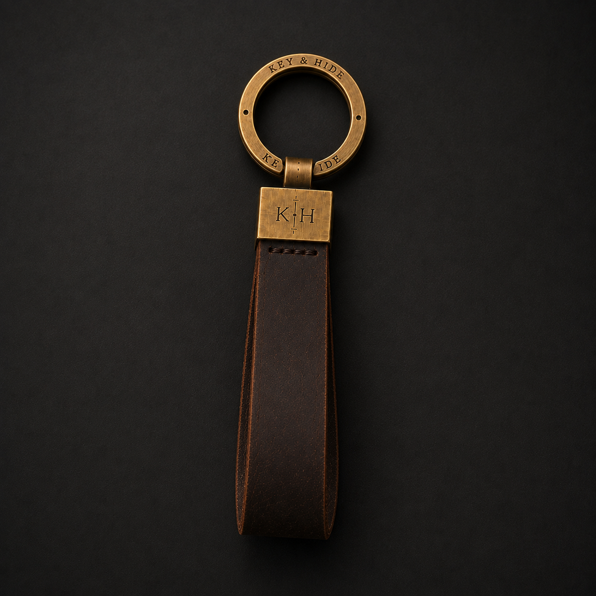 A personalized leather keychain with a dark brown leather strap and a brass-toned metal ring and connector plate engraved with the initials 'K+H' and 'MVP & RIV'.